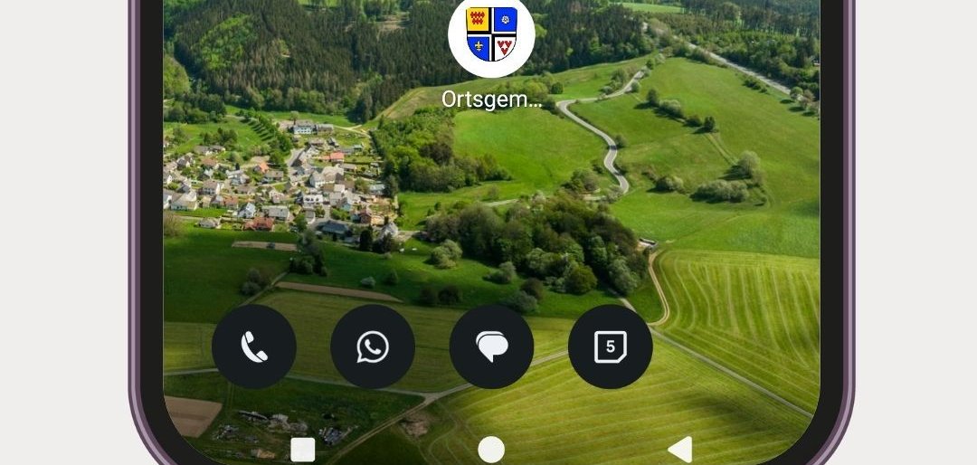 Ein Smartphone-Bildschirm zeigt den Startbildschirm eines Android-Geräts mit einem Landschaftshintergrund aus sanften grünen Hügeln, Wäldern und einem kleinen Dorf (Jammelshofen) unter blauem Himmel mit Wolken. Im unteren Drittel befindet sich ein einzelnes App-Icon mit einem viergeteilten Wappen der Ortsgemeinde Kaltenborn.