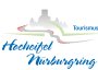 Logo mit dem Text „Hocheifel Nürburgring“ in blauer Schreibschrift und „Tourismus“ in blauer Druckschrift. Im Hintergrund eine graue Burgsilhouette, grüne Hügel und eine Straße mit rot-weißen Randstreifen.
